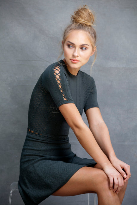 Alexa Fit and Flare Dress - VIAVAI FASHION  CLOSE UP  Profile view of a BLOND model with her hair up in a messy bun, wearing a fit andf flare knit dress in OLIVE color with beautiful textures and open knit details 