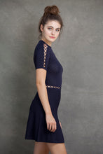 Alexa Fit and Flare Dress - VIAVAI FASHION  Profile view of a brunette model with her hair up in a messy bun, wearing a fit andf flare knit dress in Navy color with beautiful textures and open knit details  